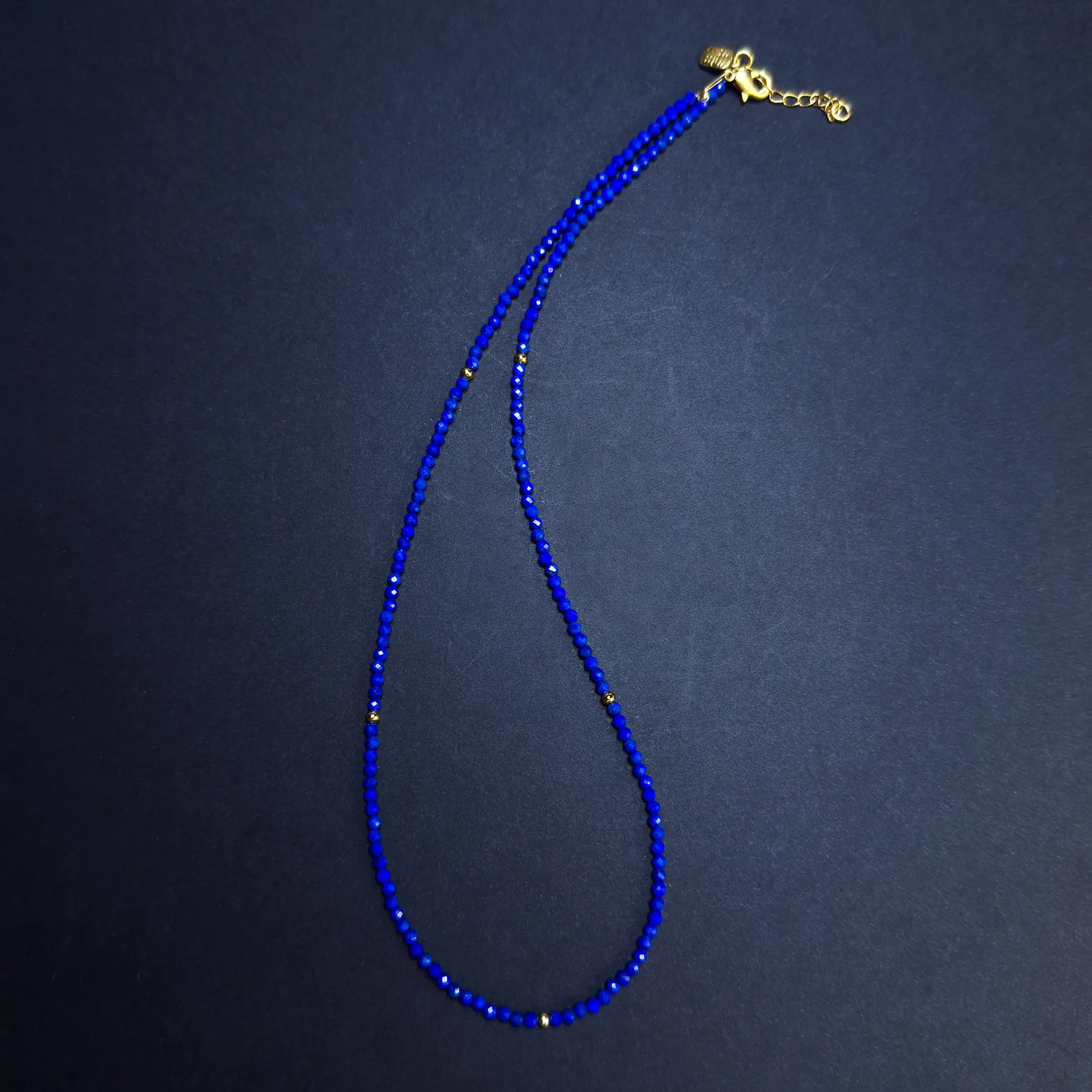 Angled full view of a cobalt blue lapis bead necklace with small gold beads