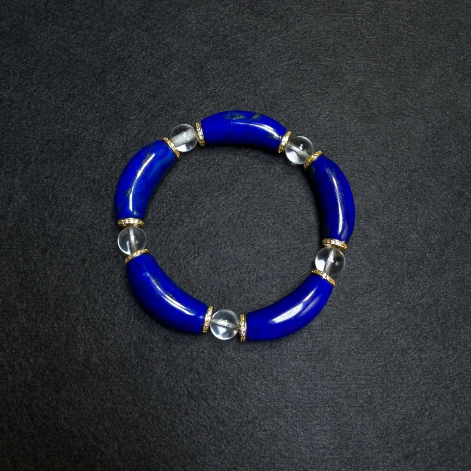 Curved lapis lazuli and clear quartz bracelet arranged on a dark background