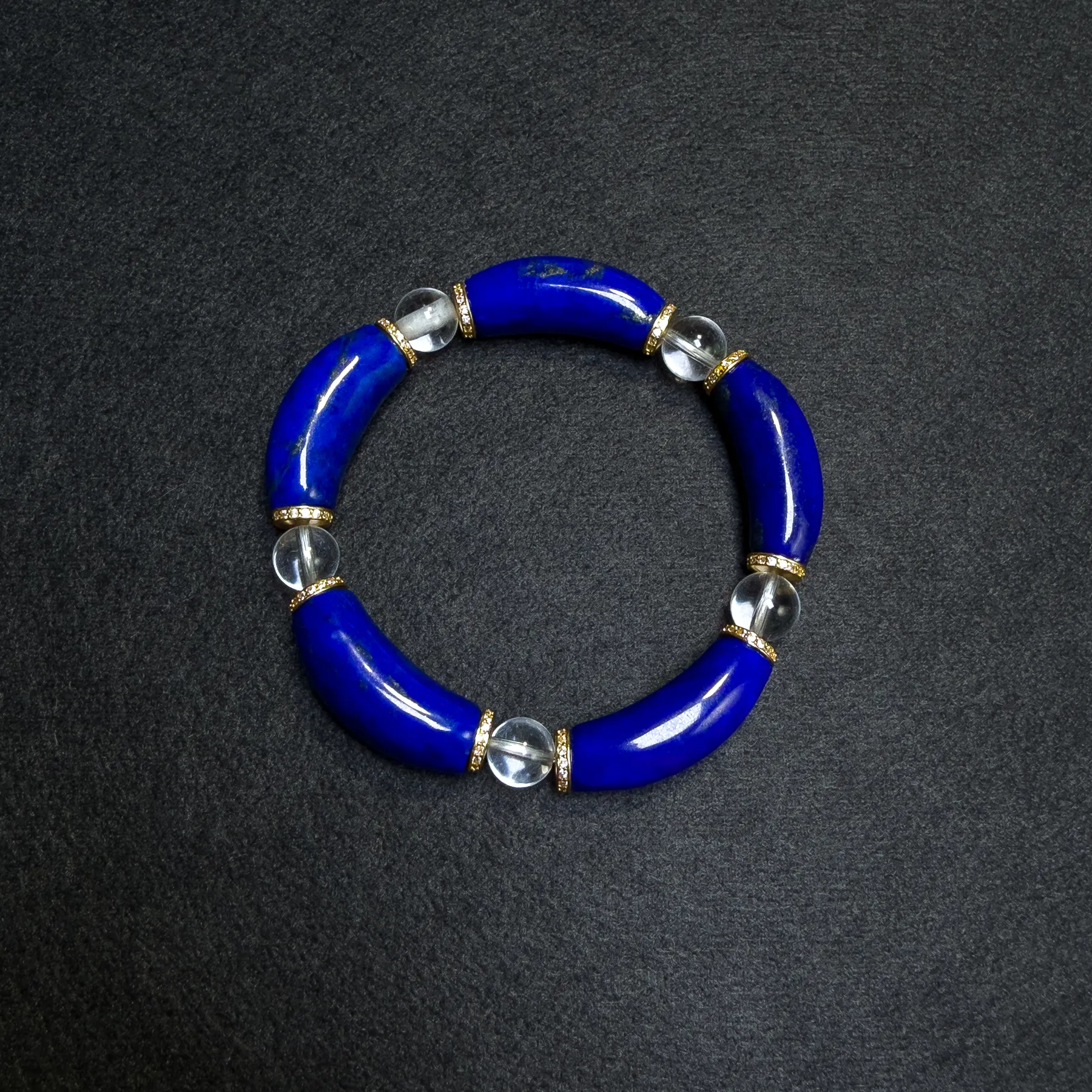 Curved lapis lazuli and clear quartz bracelet arranged on a dark background