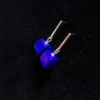 Angled lapis cube drop earrings arranged on textured black fabric