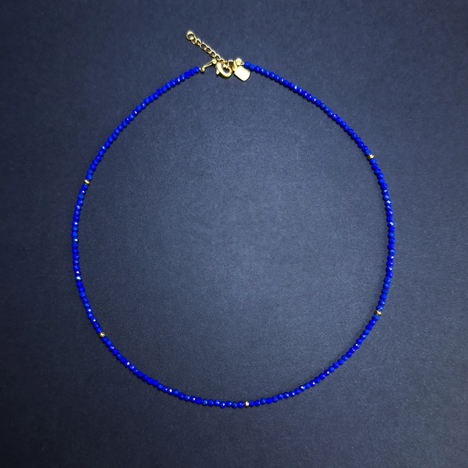 Full view of a vivid blue faceted lapis lazuli bead necklace with gold accents