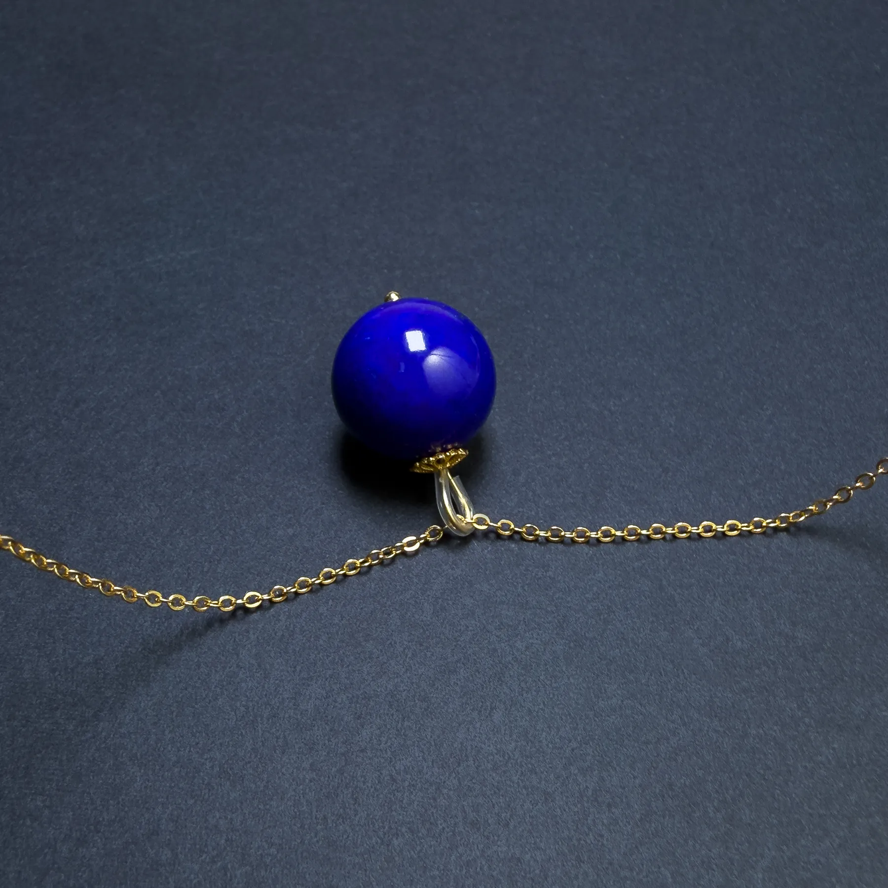 Side view of round lapis bead pendant with curved bail and chain