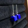 Blue lapis cube earrings displayed upright on a dark jewelry cushion