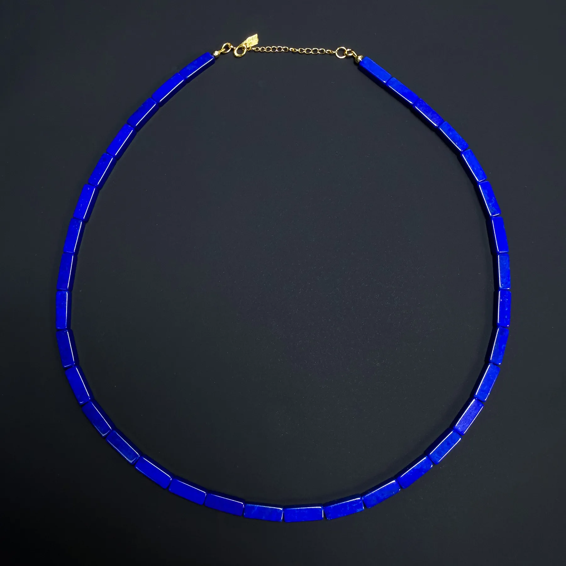 Long strand of small polished blue lapis lazuli beads arranged on a dark background