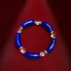 Top view of curved lapis lazuli bracelet with clear quartz beads on red fabric