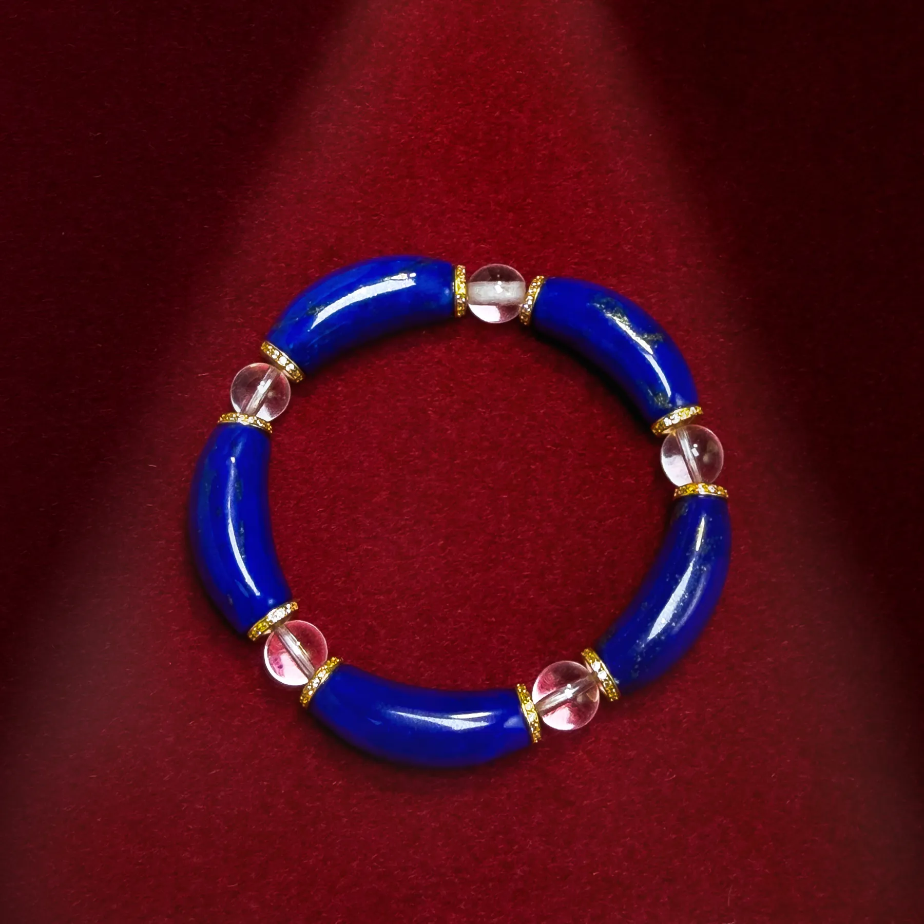 Top view of curved lapis lazuli bracelet with clear quartz beads on red fabric
