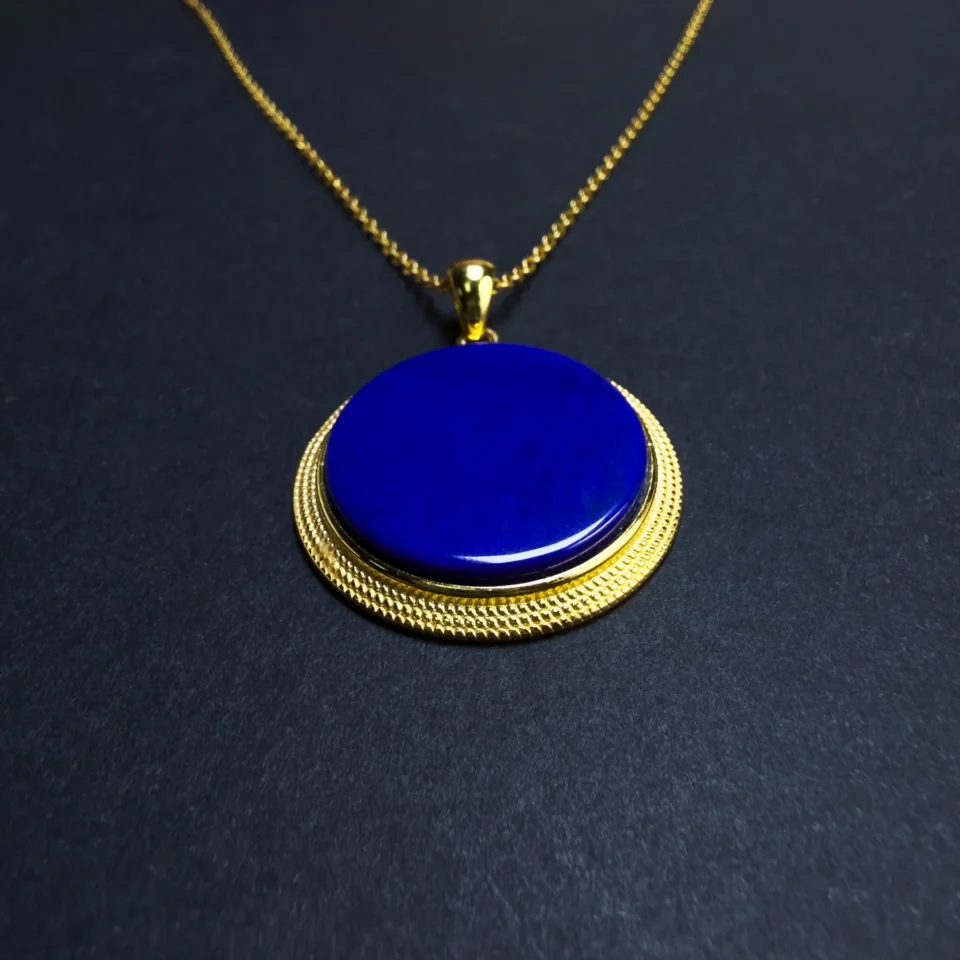 Angled close-up of blue lapis lazuli disc in textured gold-plated setting