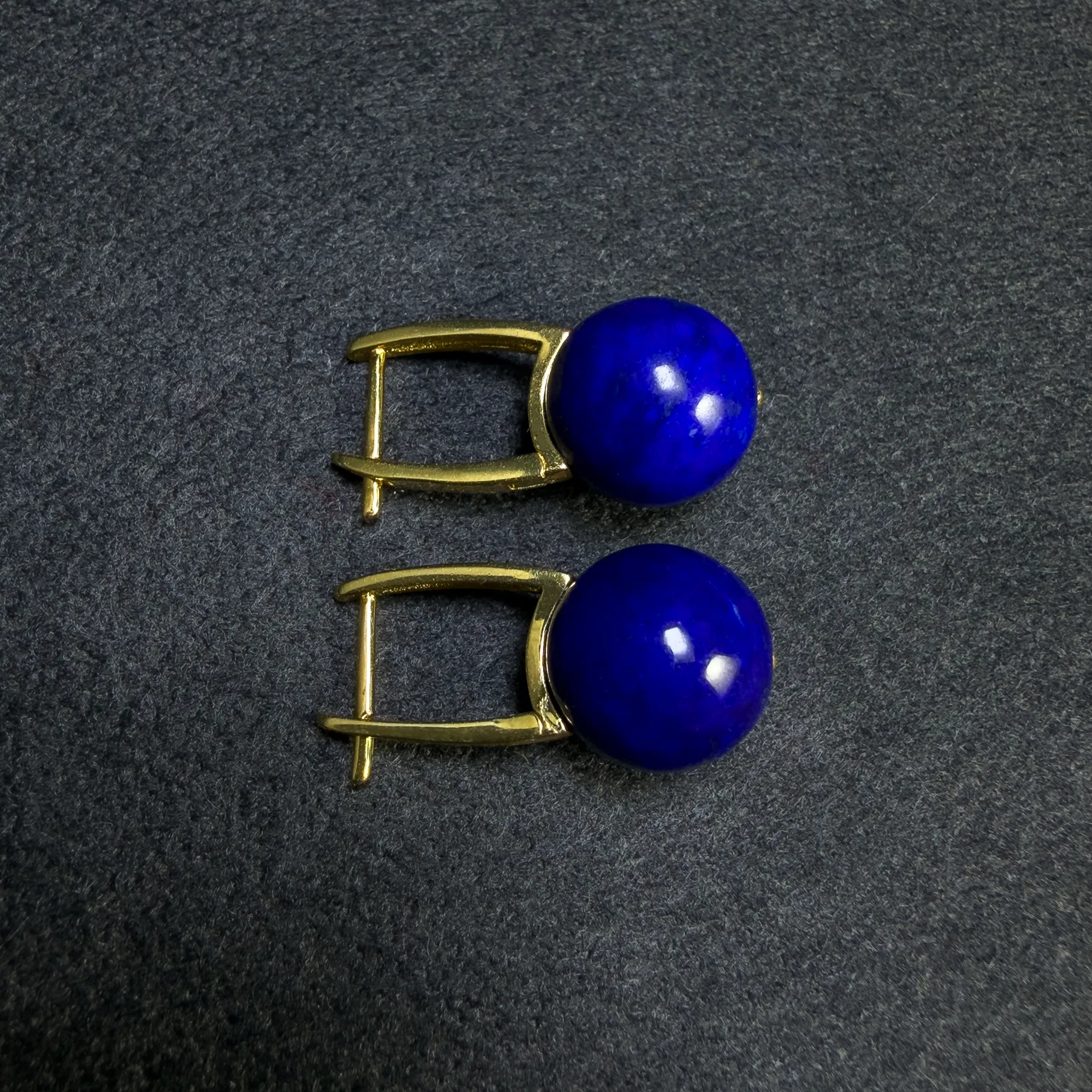 Pair of deep blue round lapis lazuli drop earrings on a dark surface