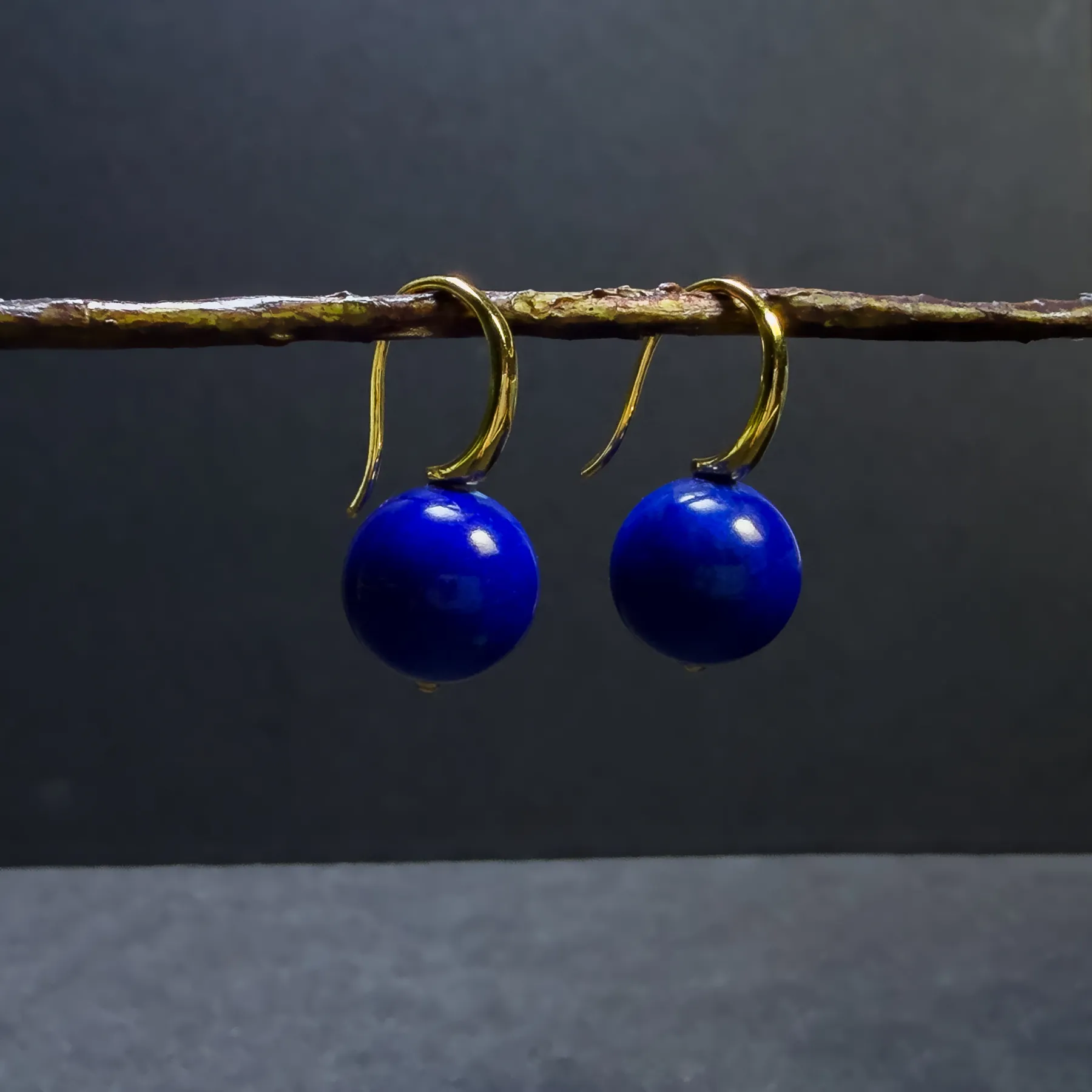 Pair of blue lapis lazuli drop earrings hanging from a natural twig