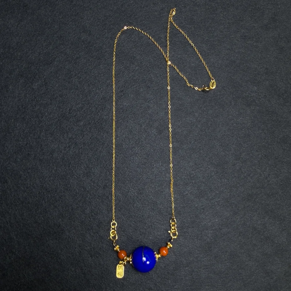 Full gold-tone chain with lapis lazuli orbit pendant on dark fabric