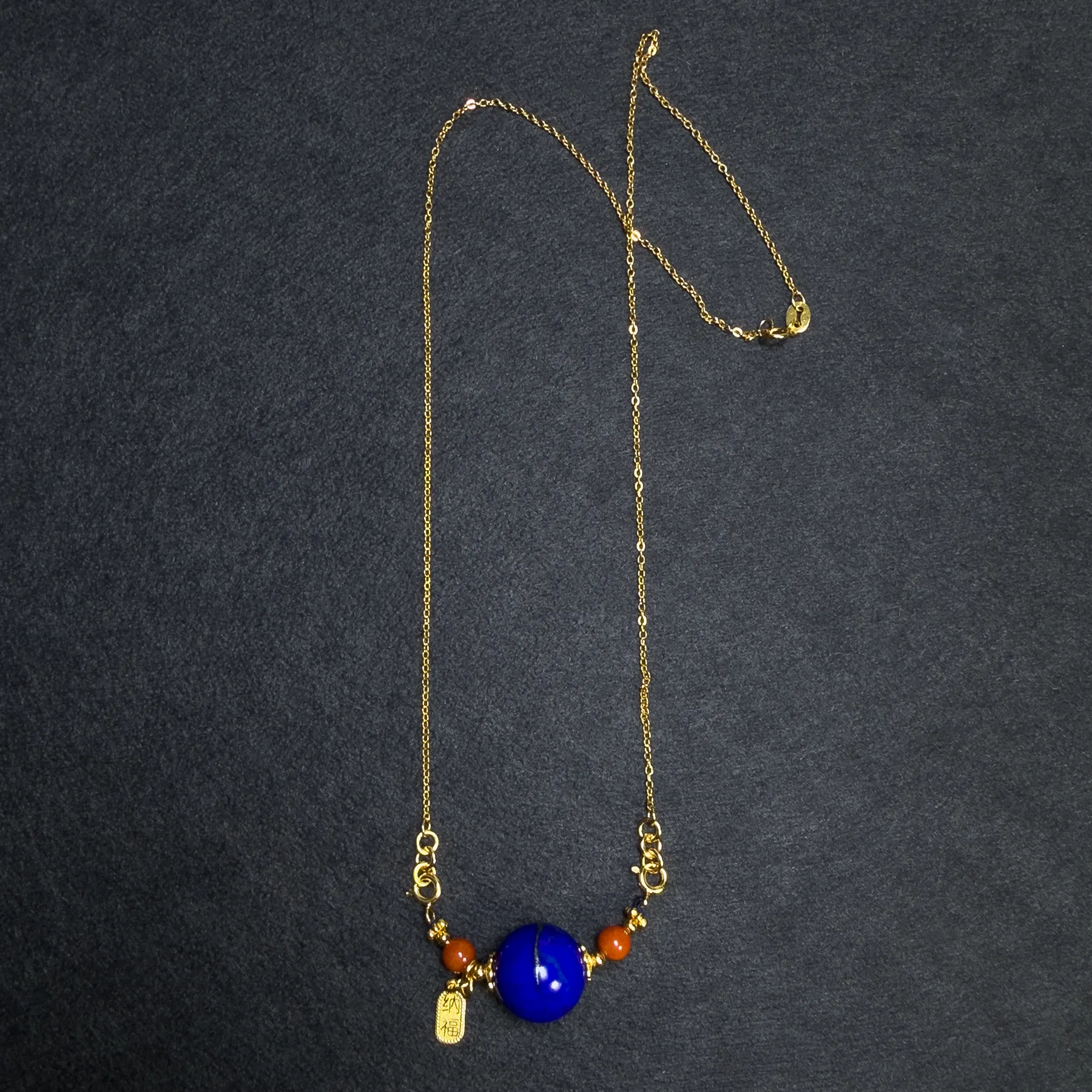 Full gold-tone chain with lapis lazuli orbit pendant on dark fabric