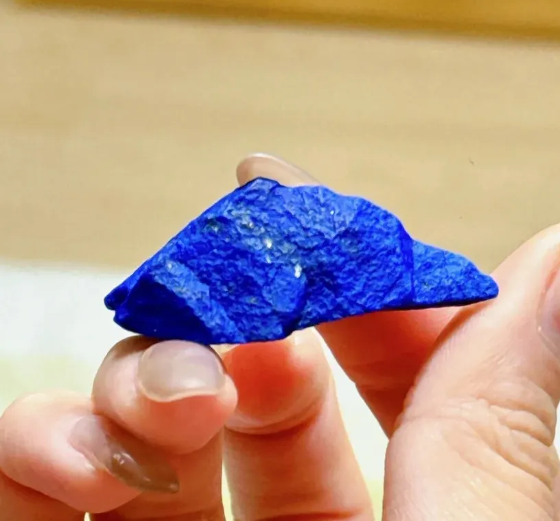 Hand holding a small rough triangular piece of blue lapis lazuli
