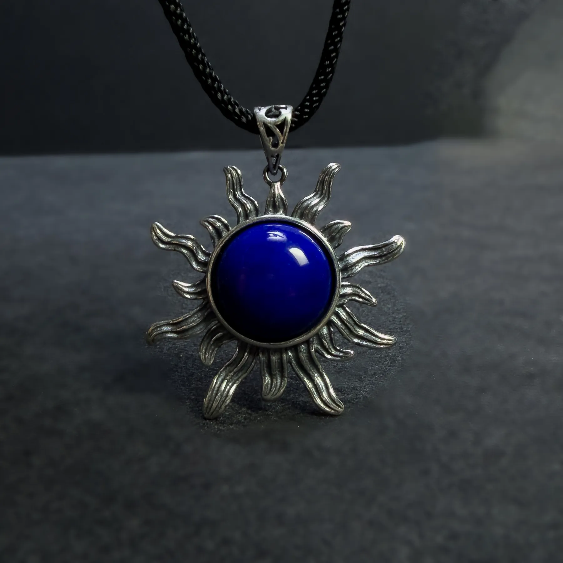 Upright lapis lazuli sun pendant displayed against a dark gray background