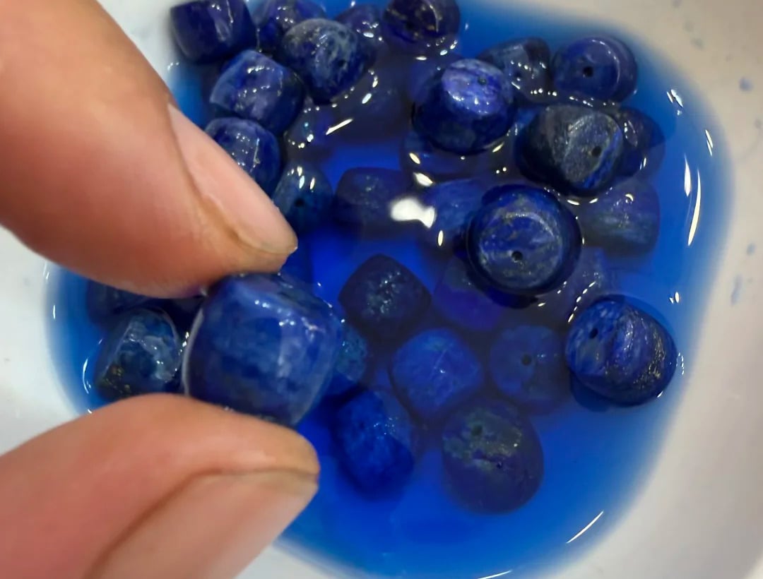 Blue lapis lazuli beads immersed in liquid during a material demonstration
