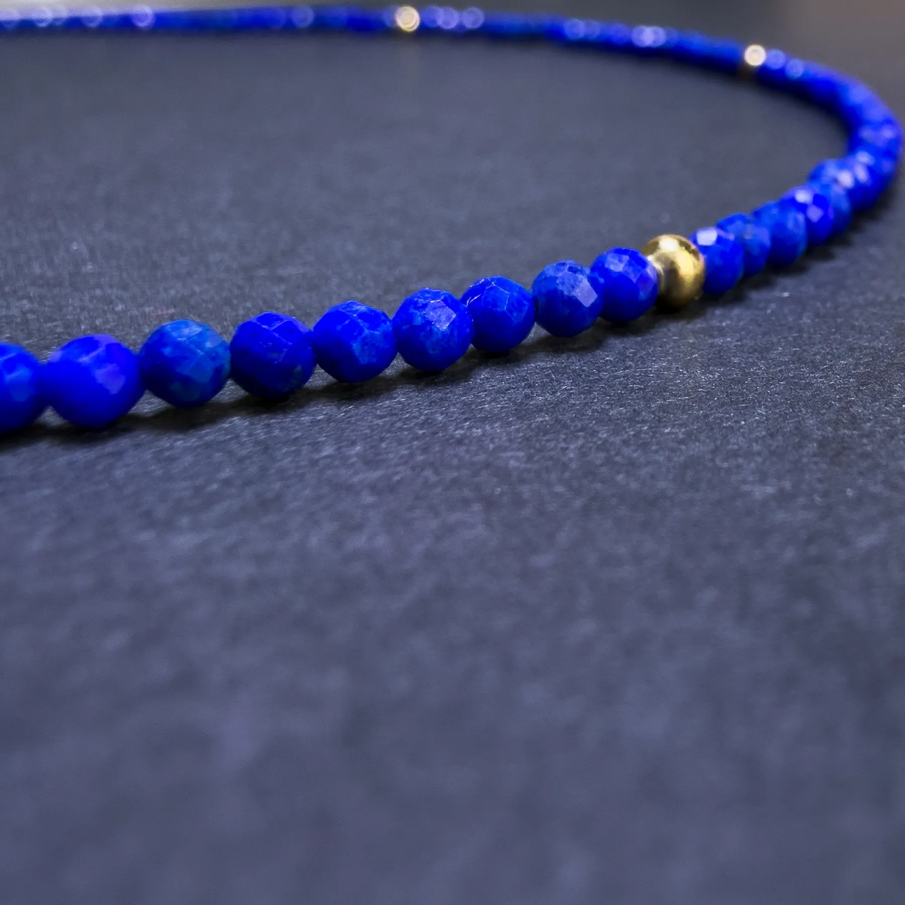 Macro detail of tiny faceted lapis lazuli beads beside one gold spacer bead