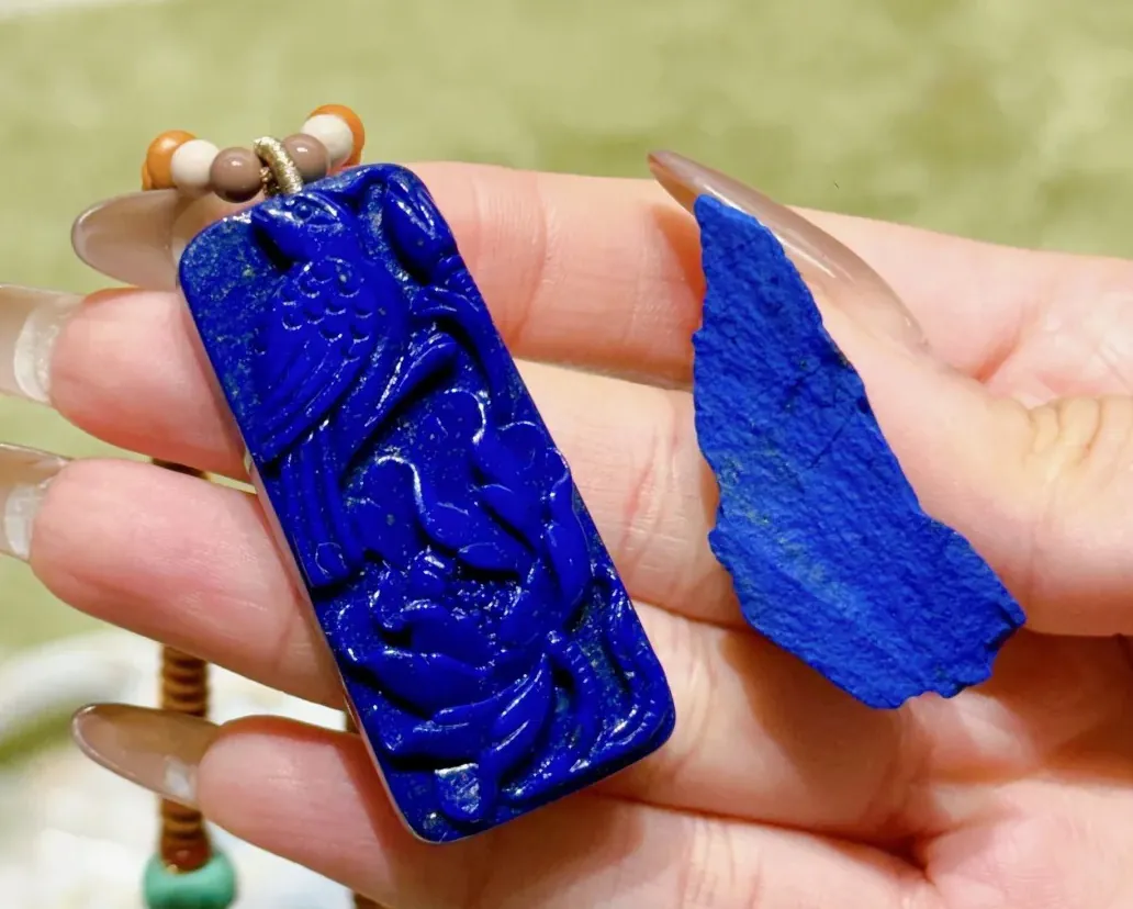 Hand holding a carved blue lapis lazuli pendant beside a rough stone fragment
