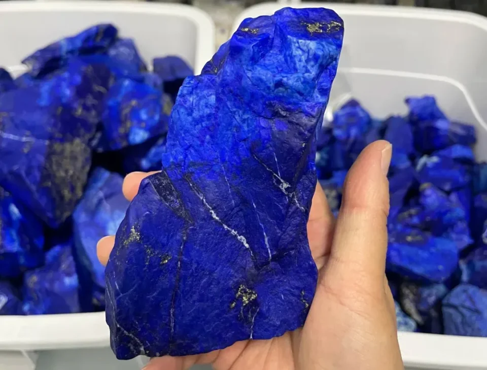 Hand holding rough deep blue lapis lazuli stones above a tray of natural pieces