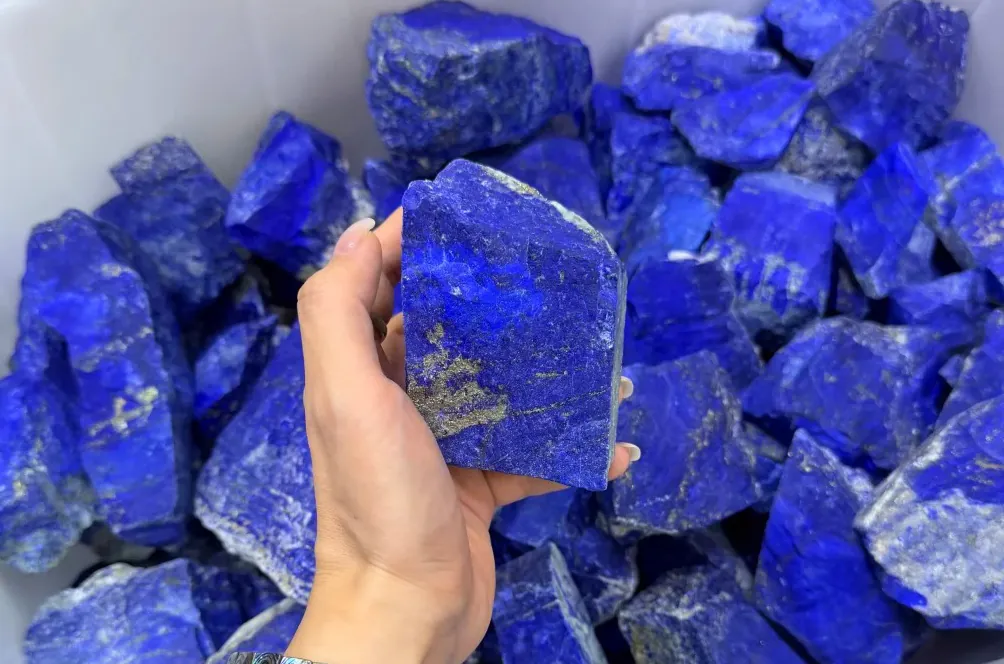 Hand holding rough lapis lazuli pieces above a large group of blue stones