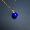 Angled round blue lapis bead pendant resting on a dark surface