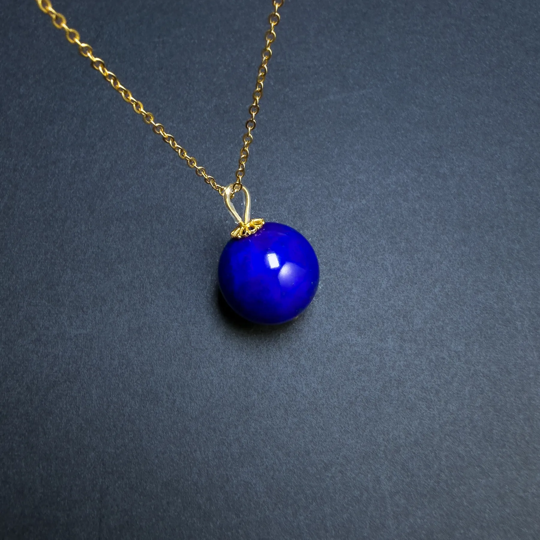 Angled round blue lapis bead pendant resting on a dark surface