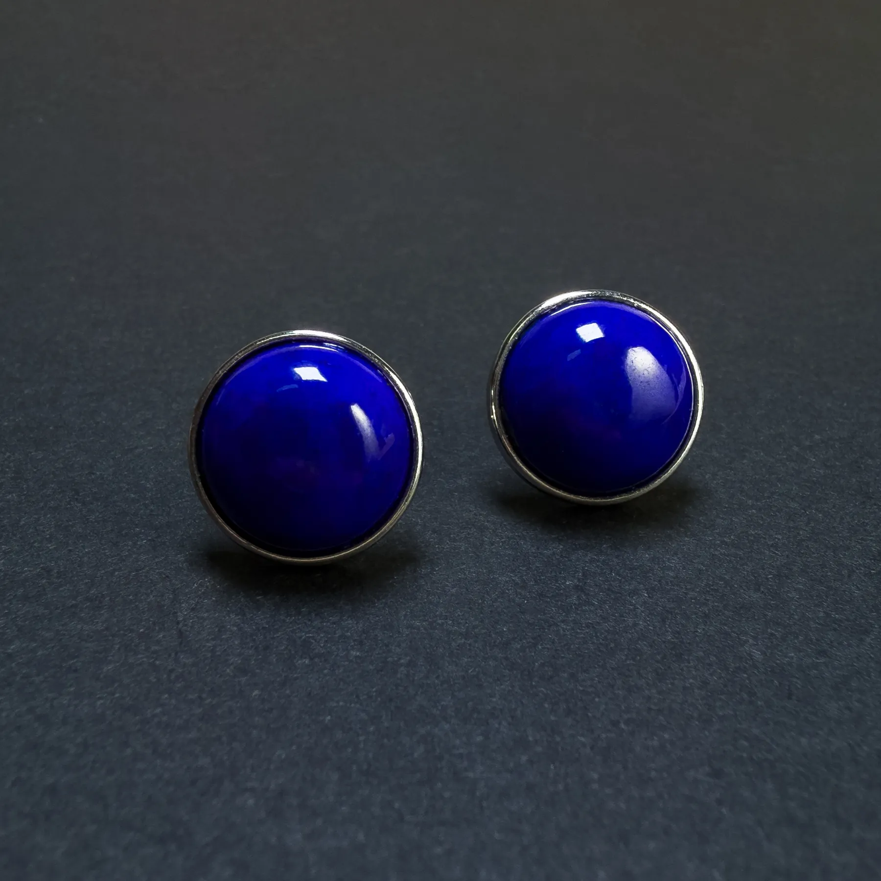 Angled front view of two round blue lapis studs with polished silver borders