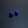 Round lapis lazuli stud earrings arranged apart on a dark surface