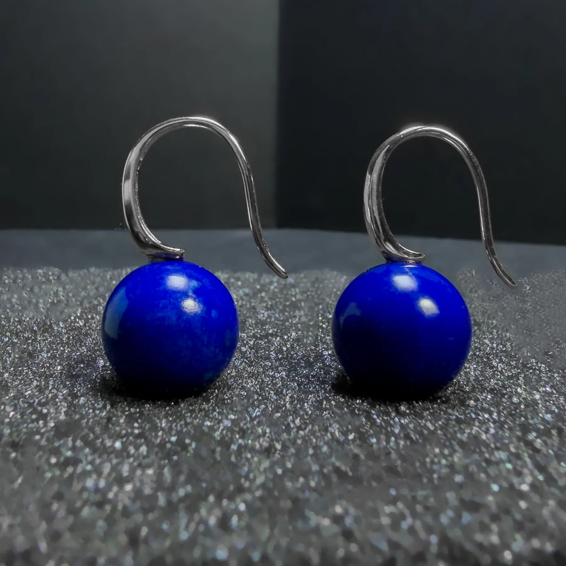 Close silver hook detail above two round lapis lazuli drop earrings