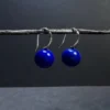 Blue lapis lazuli drop earrings with silver hooks hanging from a twig