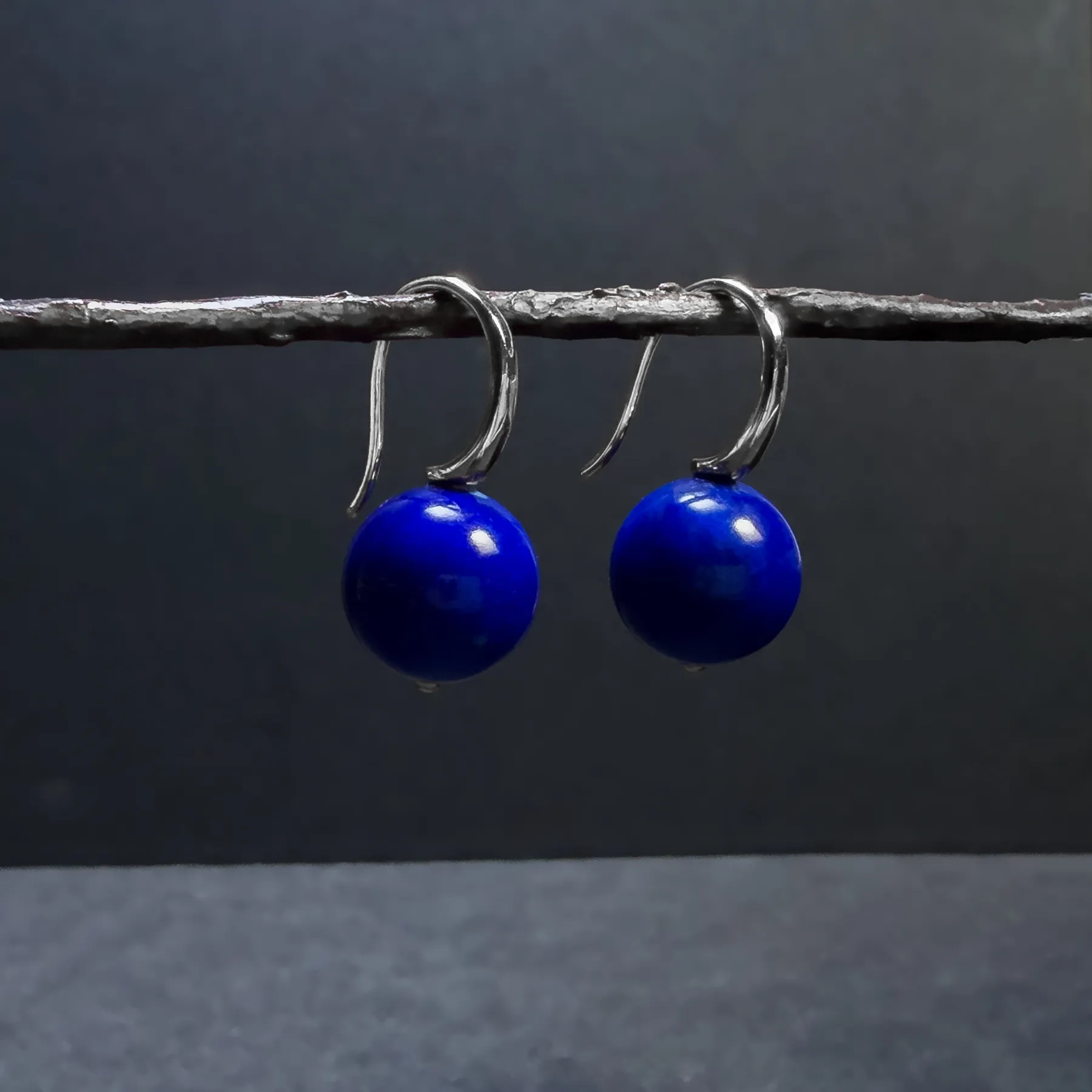Blue lapis lazuli drop earrings with silver hooks hanging from a twig