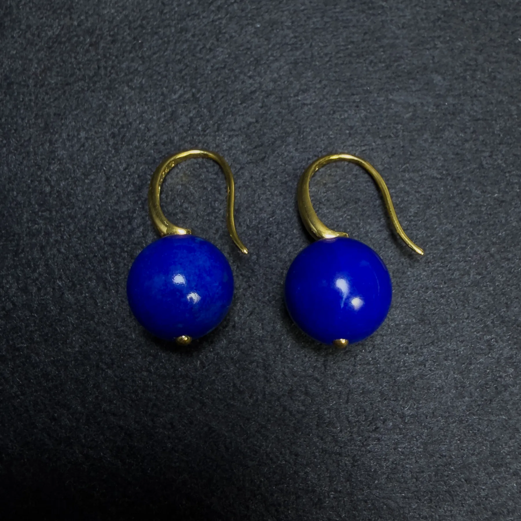 Paired untreated lapis lazuli earrings arranged side by side on dark fabric