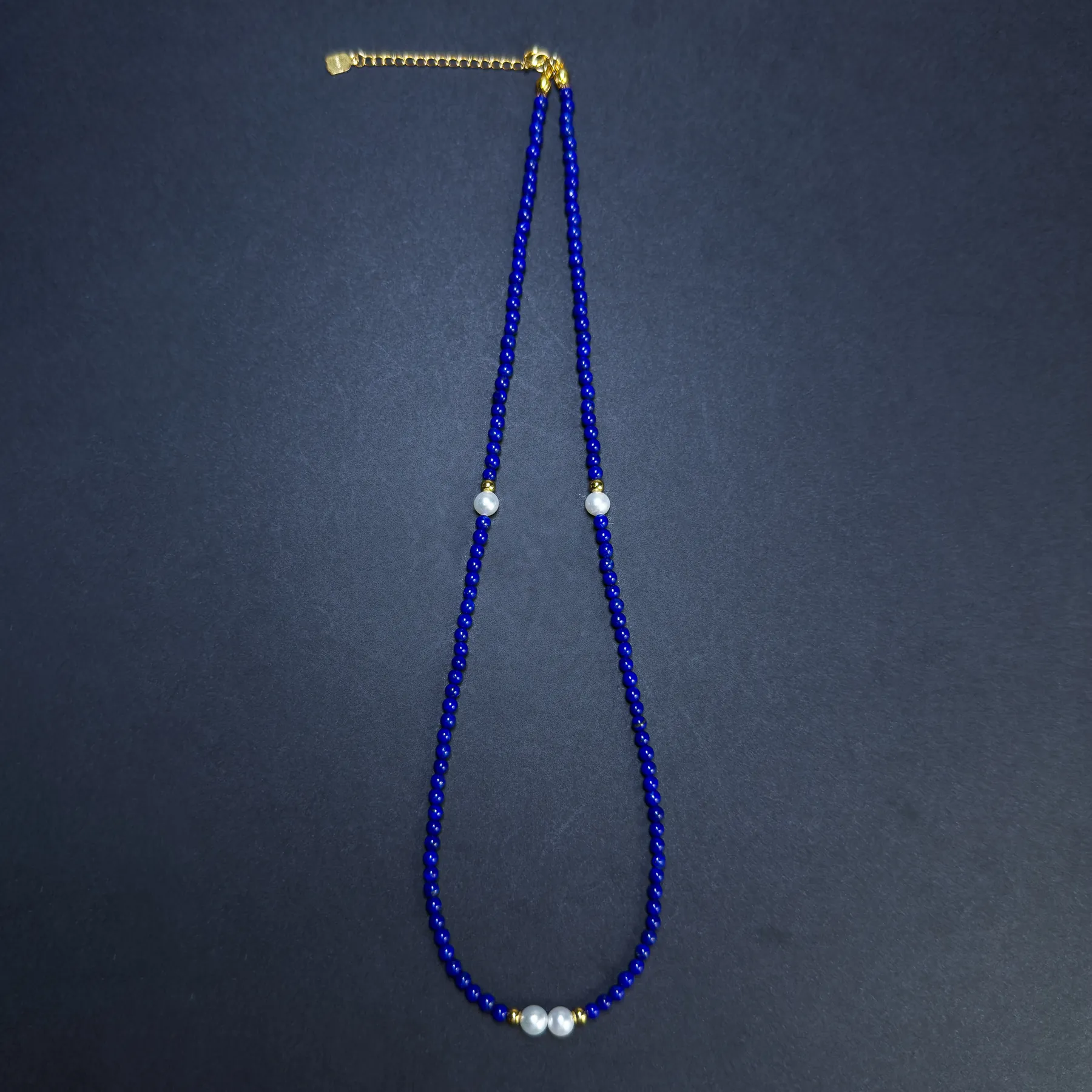 Blue bead necklace layout with side pearls and gold-toned extender