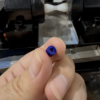 Hand holding a blue cylinder bead beside workshop shaping equipment