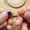 Hands holding a blue cylinder bead and removable gold-toned screw component