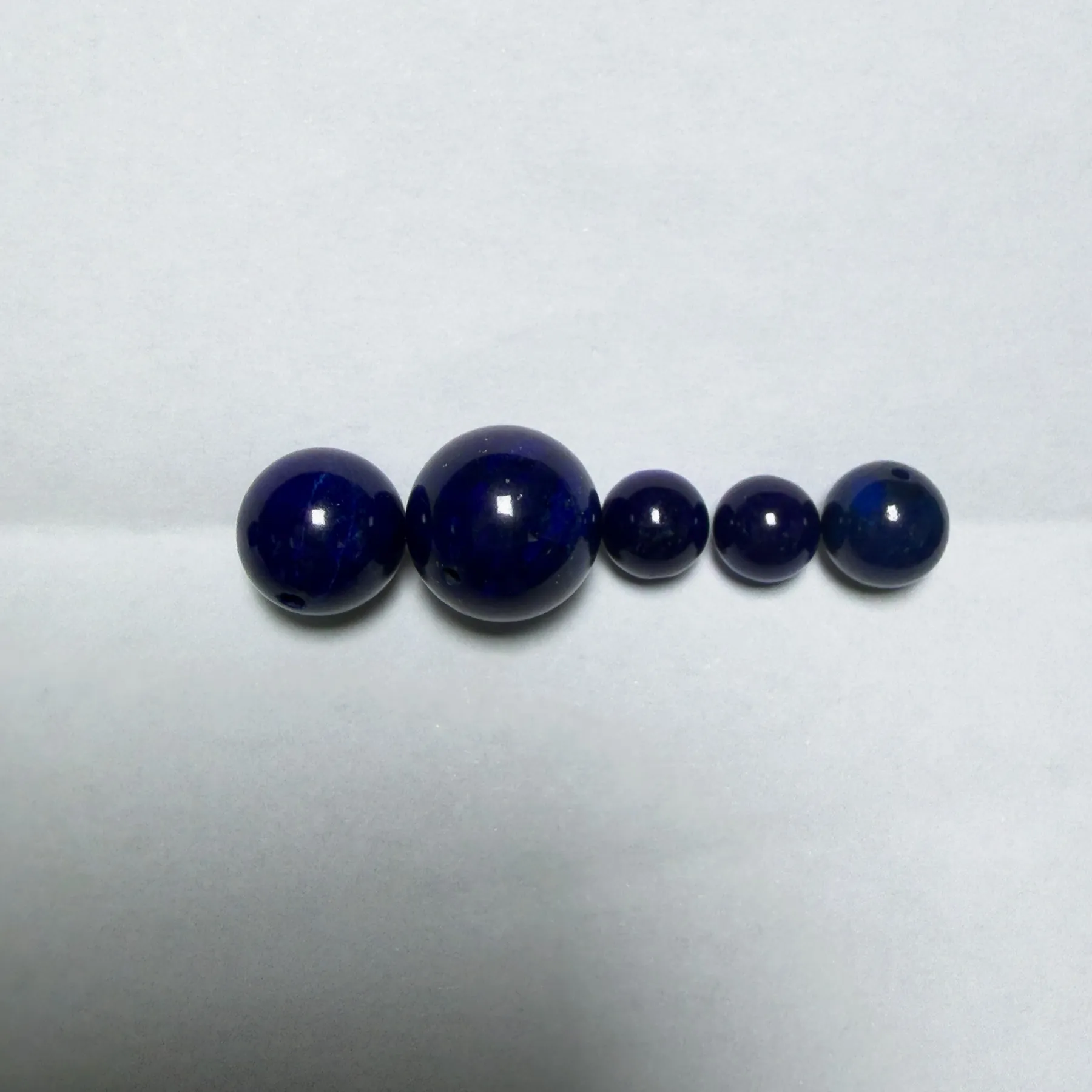 Very dark natural lapis beads appearing nearly black on a white background