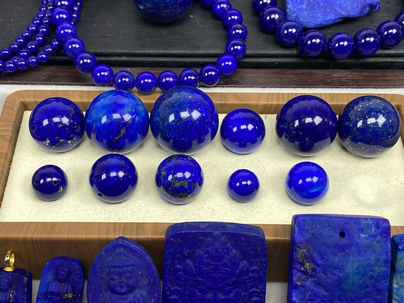 Polished lapis beads and carvings showing several shades of deep blue and mineral patterns