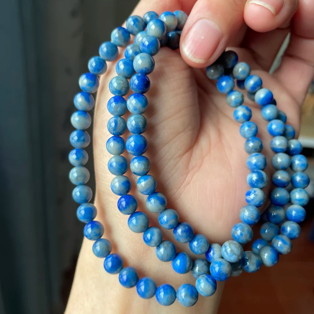Multiple denim lapis lazuli round-bead strands in soft blue and gray-blue tones held in a hand