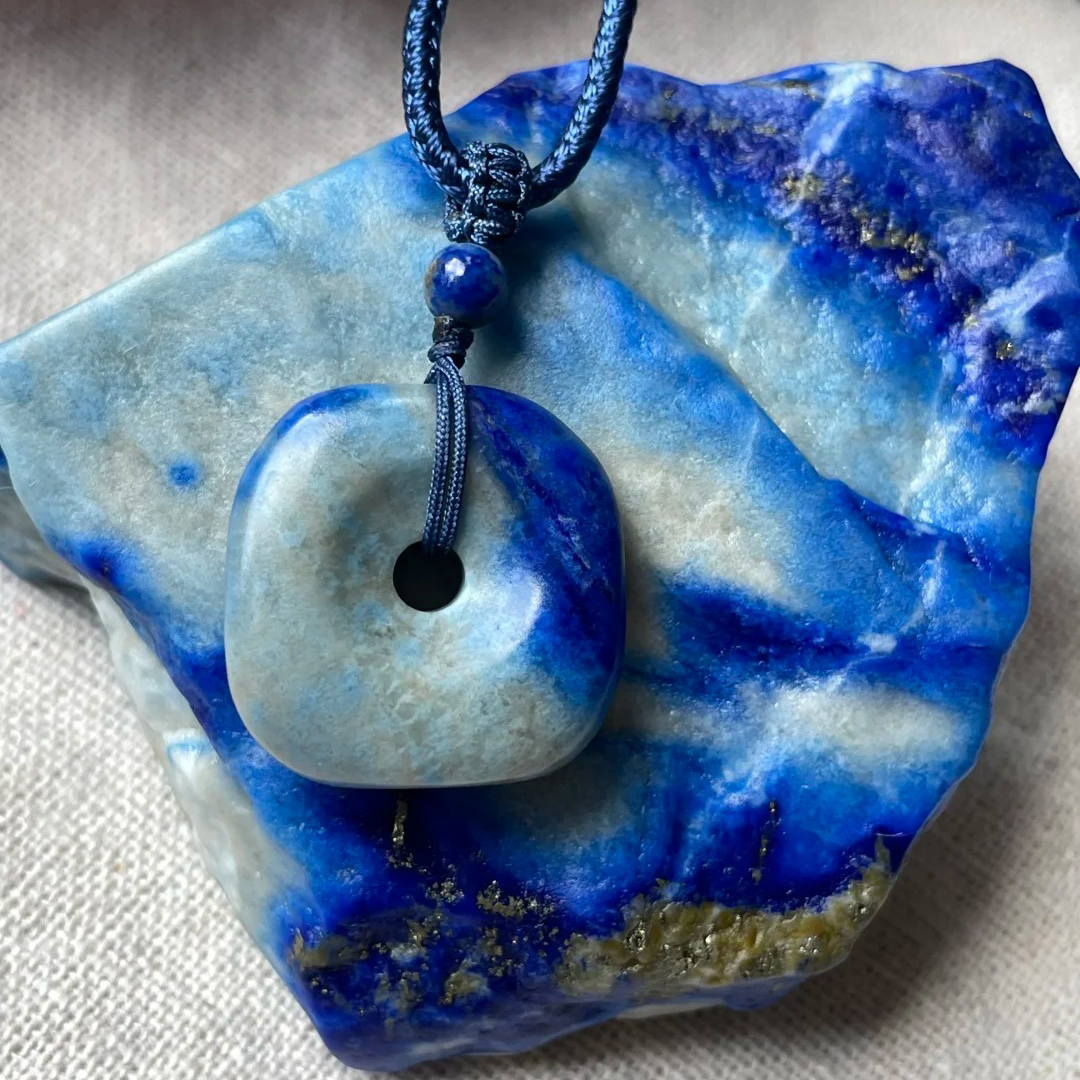 Denim lapis lazuli pendant resting on blue-and-pale lapis rough