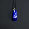 Narrow edge of the blue lapis pendant below a silver bail threaded onto black cord