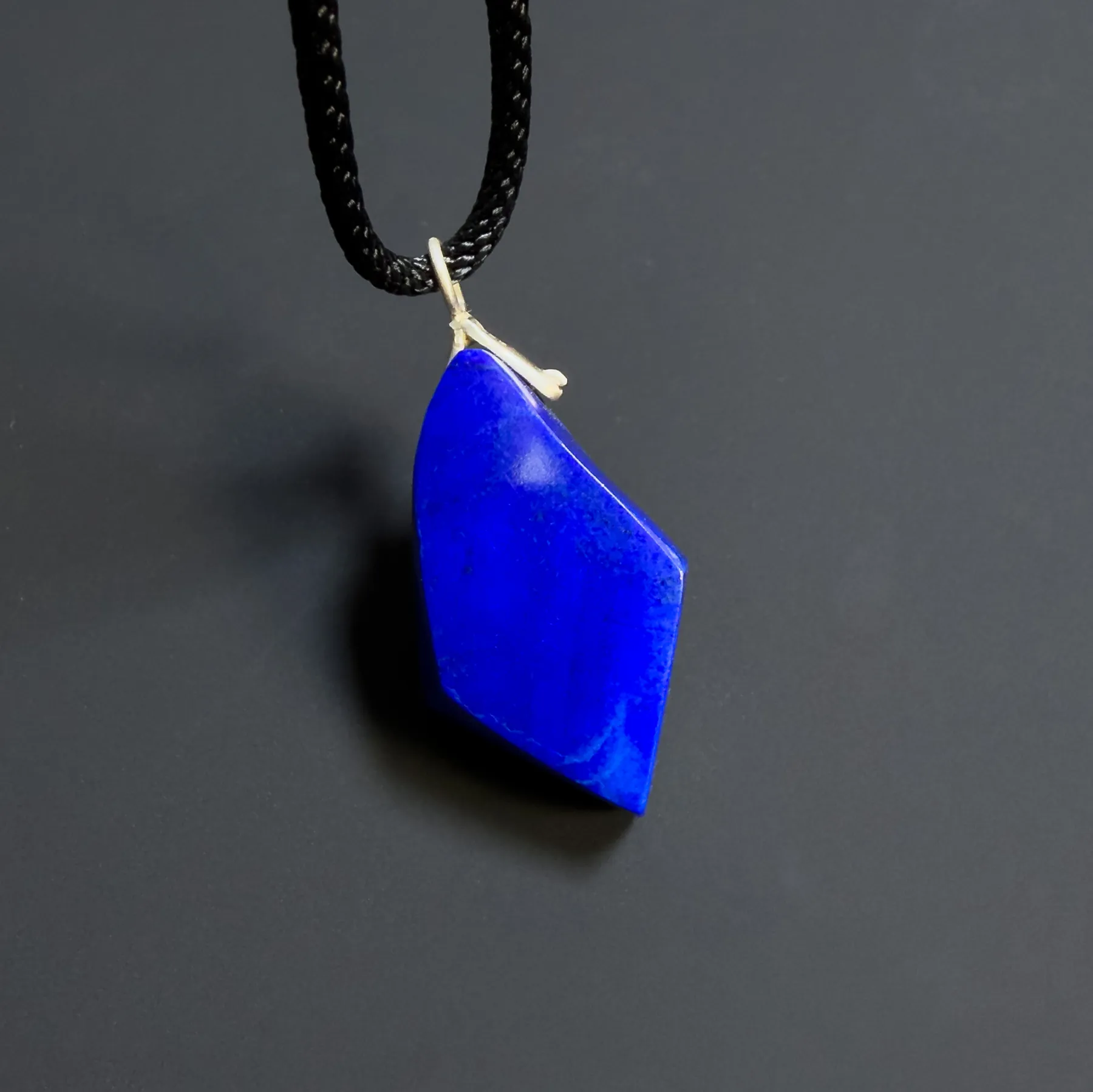 Close angled view of the lapis pendant showing its sloped polished face and side facet
