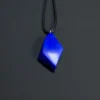 Royal-blue freeform lapis pendant hanging on a black cord against a dark background