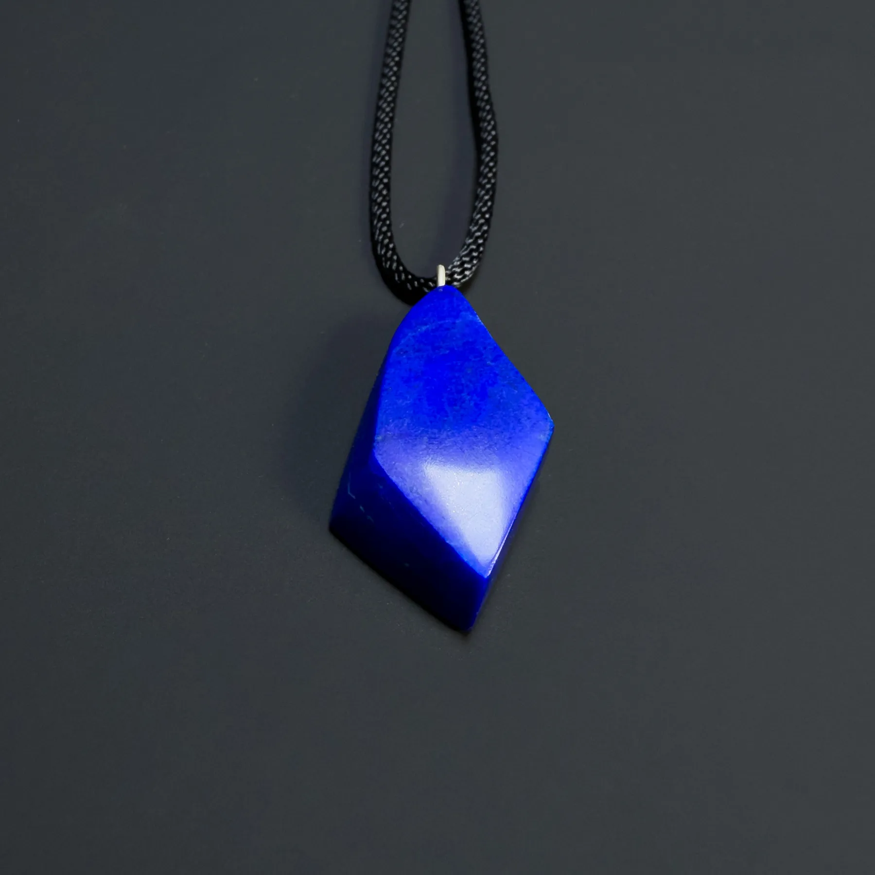 Royal-blue freeform lapis pendant hanging on a black cord against a dark background