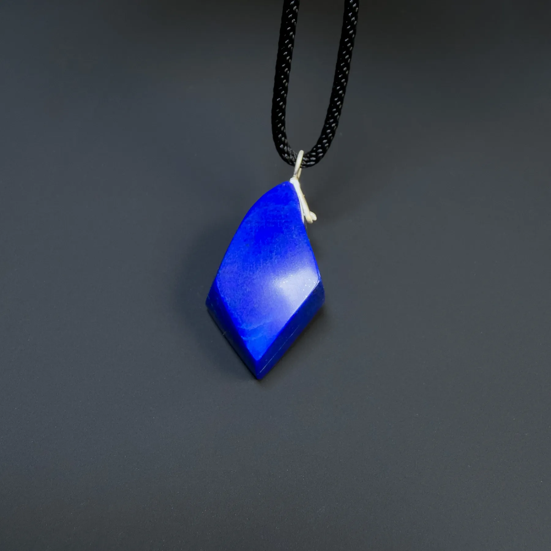 Upright front view of a faceted blue lapis pendant showing its uneven geometric outline