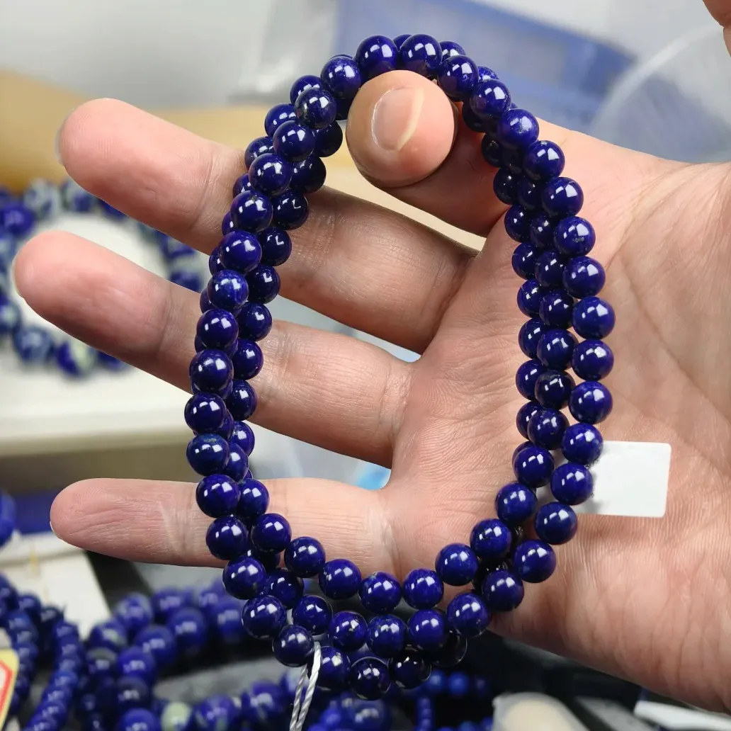 Several strands of small polished deep-blue lapis beads held in a hand