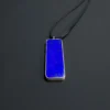Rectangular blue lapis pendant suspended on a black nylon cord against a dark background